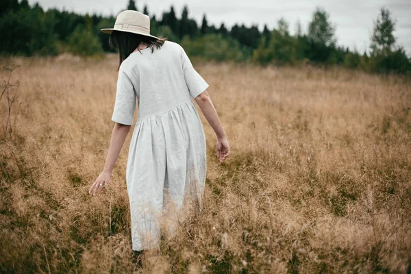 Stijlvolle meisje in linnen jurk en hoed wandelen tussen kruiden en wild — Stockfoto