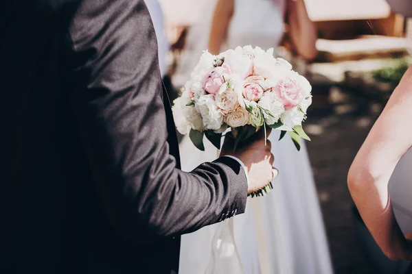 Elegante sposo in abito nero che tiene moderno bouquet da sposa di te — Foto Stock