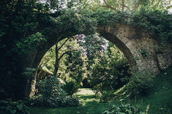 Beautiful old stone bridge with greenery in sunny botanical garden, on Borromean Islands on Lago Maggiore, Stresa city, Italy. Relaxing on on Lago Maggiore. Summer vacation in Europe