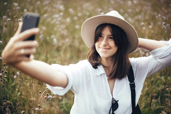 Happy hipster girl making selfie on phone among sunny wildflower — Stock Photo, Image