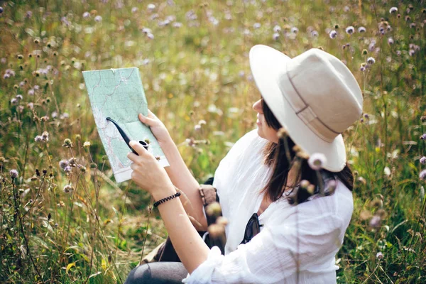 Hipster-Mädchen mit Rucksack schaut auf Landkarte und hält Holzkerne in der Hand — Stockfoto