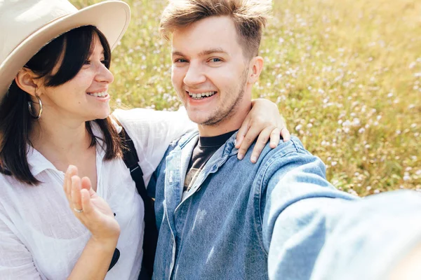 Heureux couple hipster faire selfie dans ensoleillé prairie de fleurs sauvages, t — Photo