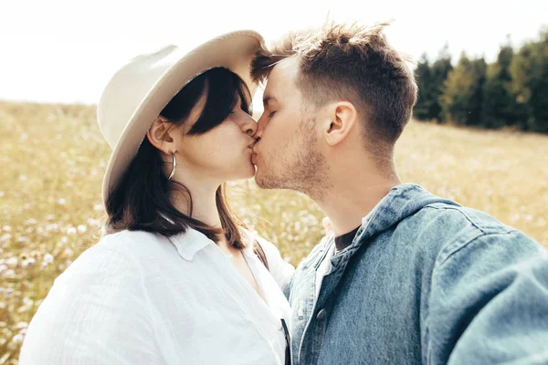 Feliz hipster casal fazendo selfie e beijos na ensolarada montanha — Fotografia de Stock