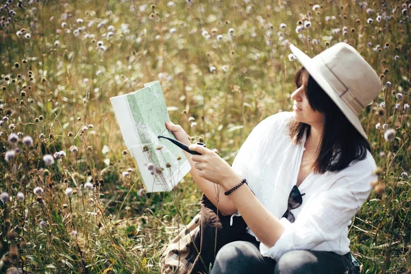 Hipster chica con tubo de madera mirando el mapa y sentado en el sol —  Fotos de Stock