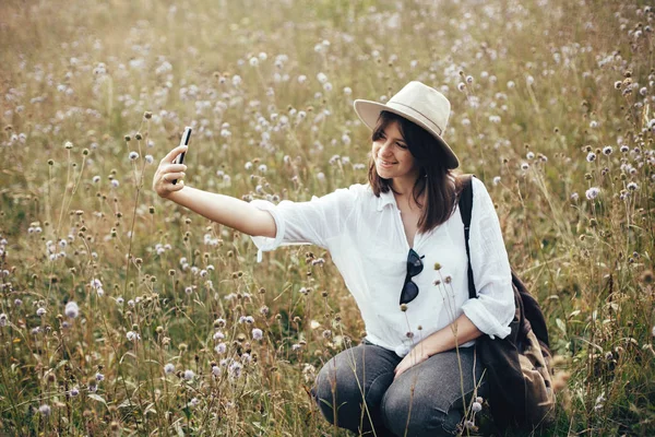 Счастливая девушка-хипстер делает селфи по телефону среди солнечных полевых цветов — стоковое фото
