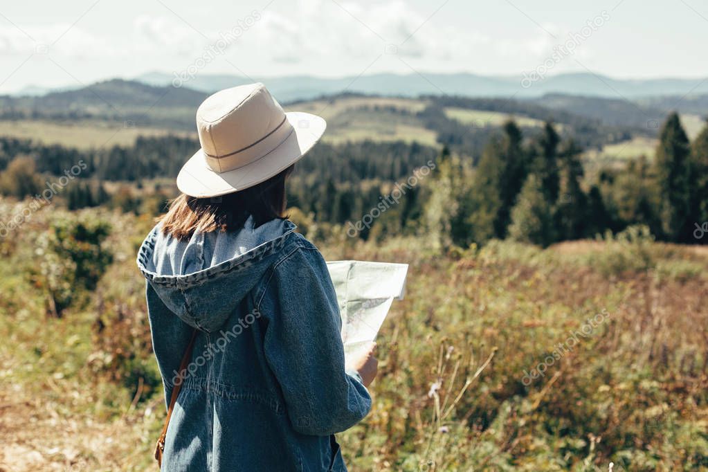 Stylish hipster girl holding map and traveling in sunny mountain