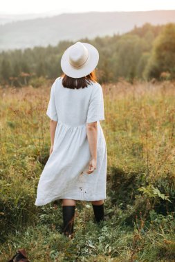 Şık boho kız atmosferik gün batımında güneşli çayırda yürüyüş