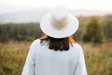 Şık boho kız atmosferik gün batımında güneşli çayırda yürüyüş