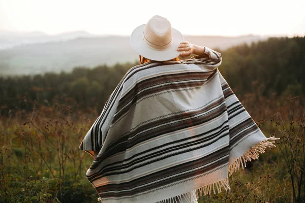 Mujer hipster feliz en poncho y sombrero disfrutando de viajar en incluso —  Fotos de Stock