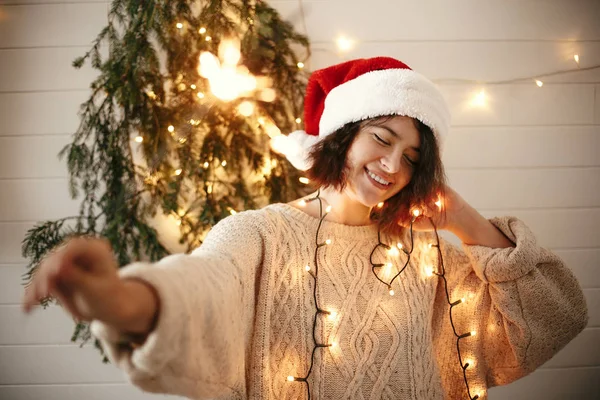 Stylish happy girl in santa hat holding sparkler on background — Stock Photo, Image