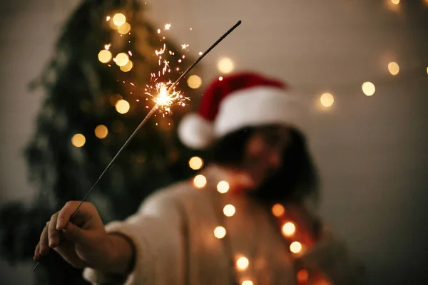 Big sparkler burning in hand of stylish girl in santa hat on bac — Stock Photo, Image