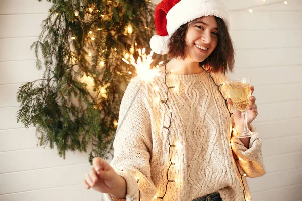 Stylish happy girl in santa hat holding sparkler and champagne g — Stock Photo, Image
