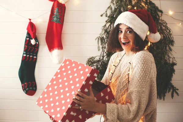 Stylish surprised girl in santa hat opening gift box in christma — Stock Photo, Image