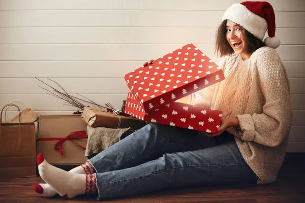 Stylish happy girl in santa hat opening christmas gift box with — Stock Photo, Image