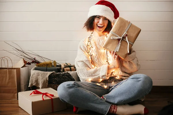 Stylish happy girl in santa hat holding christmas gift box on ba — Stock Photo, Image