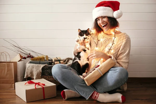 Stylish happy girl in santa hat smiling and playing with cute ca — Stock Photo, Image