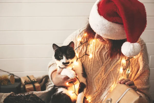 Élégant heureux fille dans santa chapeau jouer avec mignon chat dans festive — Photo