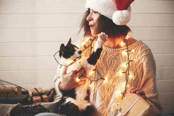 Mignon chat jouer avec santa chapeau sur élégant heureux fille dans festive — Photo