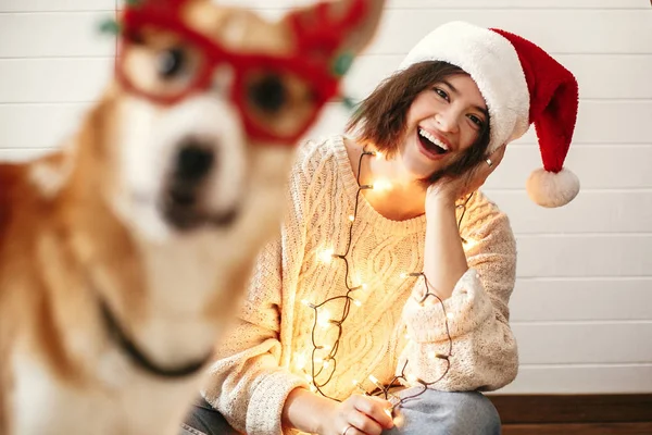Stylish girl smiling in santa hat and christmas lights and looki — Stock Photo, Image