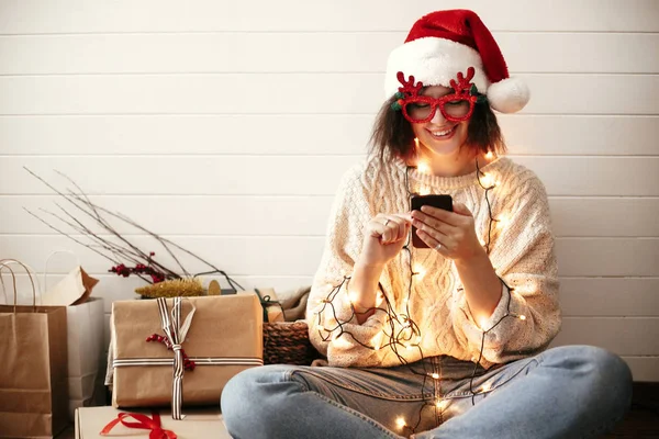 Stylish happy girl in festive glasses with reindeer horns holdin — Stock Photo, Image