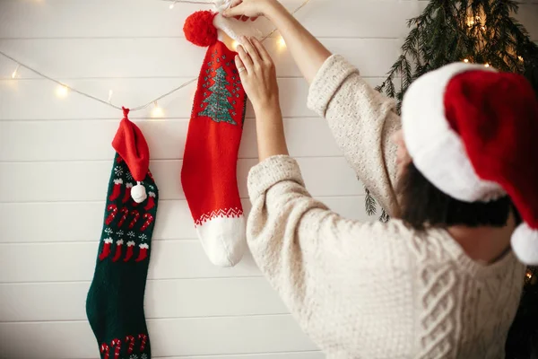 Stylish girl in cozy sweater and santa hat decorating room for c — Stock Photo, Image
