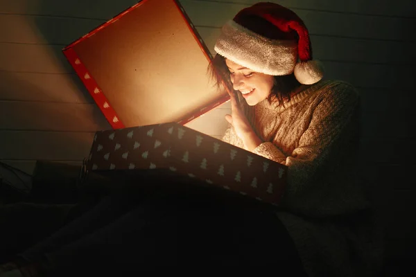 Stylish happy girl in santa hat and cozy sweater opening christm — Stock Photo, Image