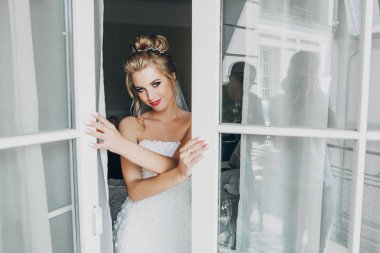 Şık mutlu gelin poz ve pencere yakınında yumuşak ışıkta gülümseyen