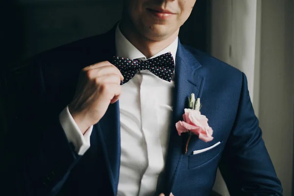 Stylish groom in blue suit with boutonniere with pink rose holdi — Stock Photo, Image