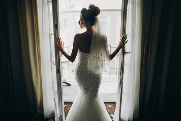 Silhouette der stilvollen Braut öffnet Fensterbalkon in sanftem Licht — Stockfoto