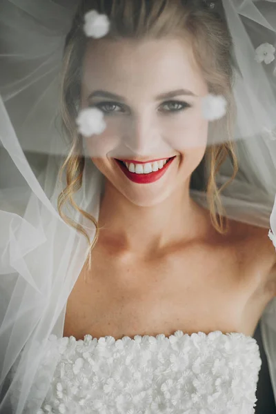 세련된 행복한 신부는 베일 아래 포즈를 취하고 부드러운 빛에 미소 — 스톡 사진