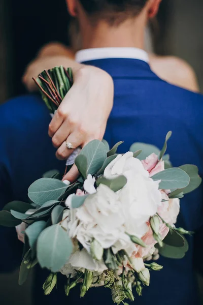 スタイリッシュな花嫁は花束を持ち、cで優しく新郎の首を抱きしめる — ストック写真