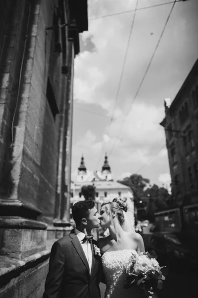日当たりの良い街で歩いてキスするスタイリッシュな幸せな花嫁と新郎 — ストック写真