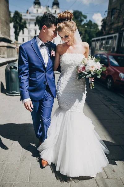 Elegante novia feliz y novio caminando y sonriendo en la ciudad soleada —  Fotos de Stock