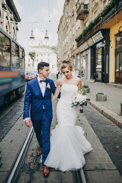Stylish happy bride and groom walking and smiling in sunny city — Stock Photo, Image