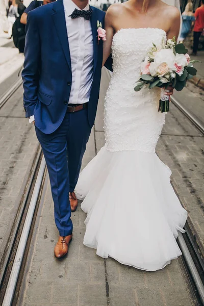 Stilvolle Braut mit Strauß und Bräutigam zu Fuß im sonnigen europäischen c — Stockfoto
