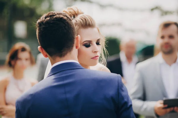 Noiva elegante e noivo gentilmente abraçando durante o matrimônio perto de se casar — Fotografia de Stock