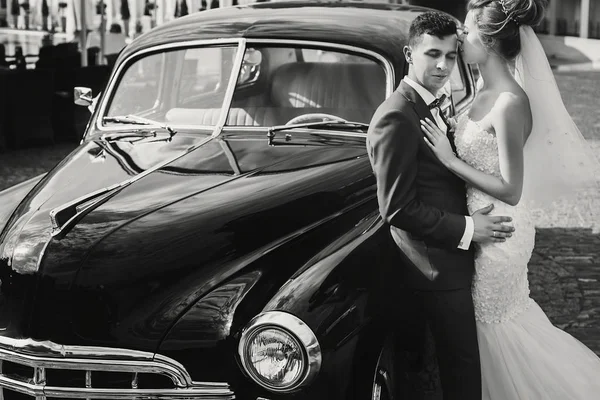 Bergaya bahagia pengantin pria dan wanita berciuman di mobil retro hitam tua. Pergi! — Stok Foto