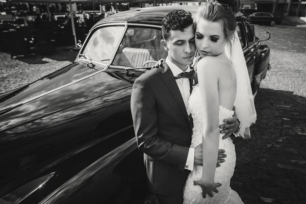 Elegante novia feliz y novio abrazando en el viejo coche retro negro . —  Fotos de Stock