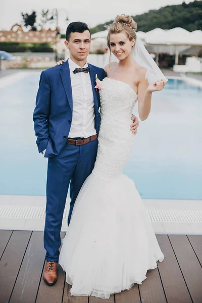 Stílusos boldog menyasszony és a vőlegény pózol a medencében kék víz esküvői — Stock Fotó