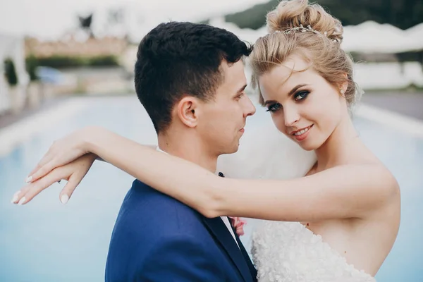 Elegante novia feliz y novio abrazándose en la piscina de agua azul a nosotros —  Fotos de Stock