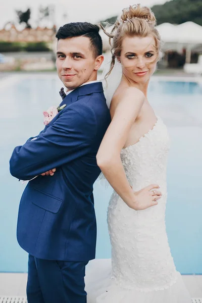 Stylish happy bride and groom posing at pool blue water at weddi — Stock Photo, Image