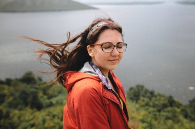 Kırmızı yağmurluk ve rüzgarlı saçlı gezgin kız üzerinde duran