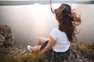 Şapka ve rüzgarlı saçlı gezgin hipster kız ro üstüne oturan