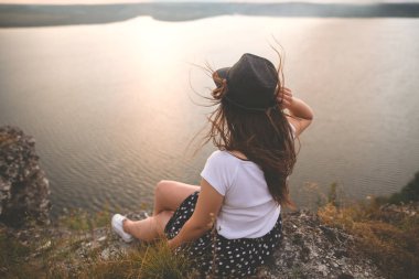 Şapka ve rüzgarlı saçlı gezgin hipster kız ro üstüne oturan