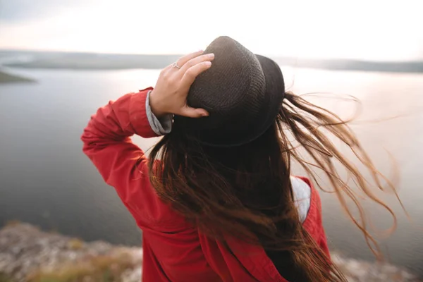 Menina viajante em chapéu e com cabelo ventoso em pé ao sol da noite — Fotografia de Stock