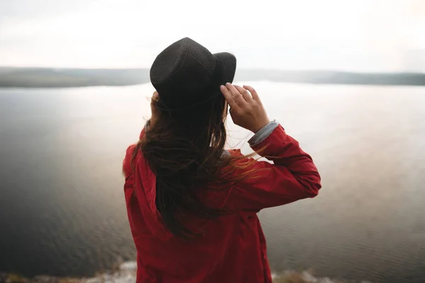 Traveler flicka i hatt och med blåsigt hår stående på toppen av rock — Stockfoto