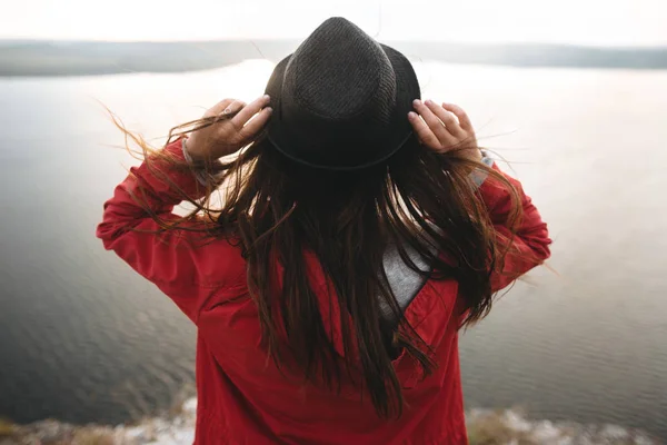 Menina viajante em chapéu e com cabelo ventoso em pé no topo da rocha — Fotografia de Stock