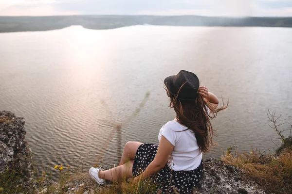 Şapka ve rüzgarlı saçlı gezgin hipster kız ro üstüne oturan