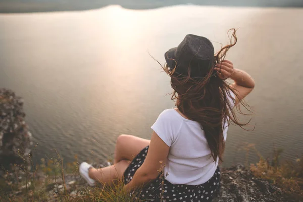 Traveler hipster flicka i hatt och blåsigt hår sitter ovanpå ro — Stockfoto