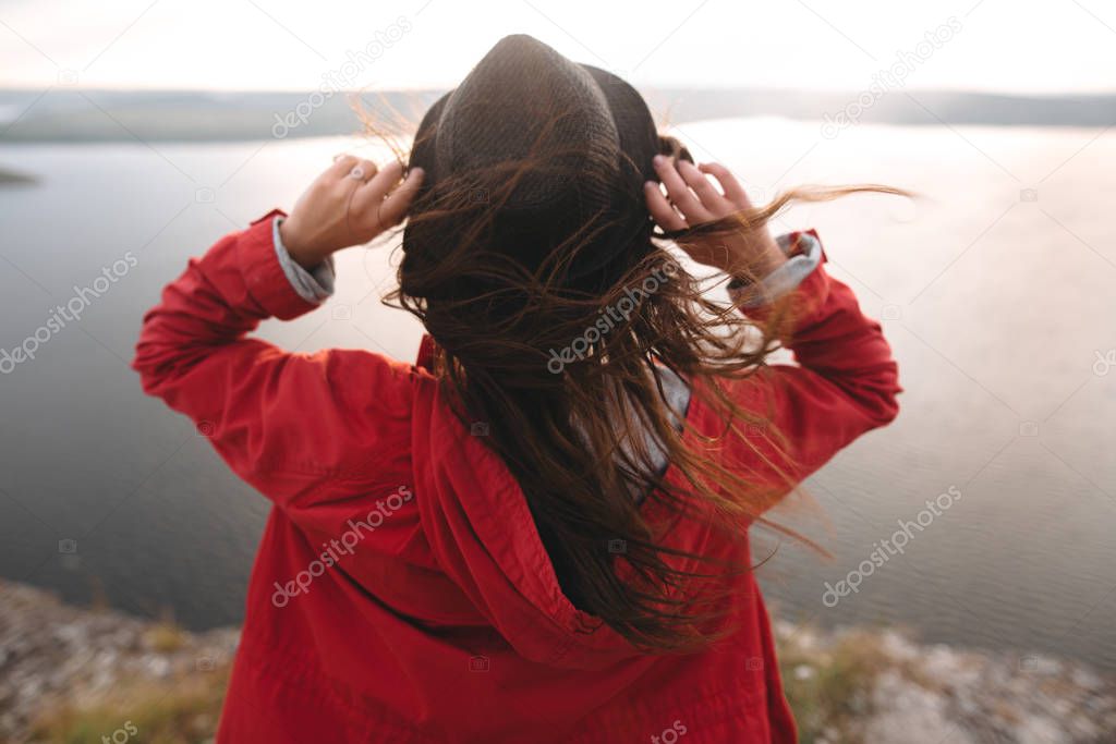 Traveler girl in hat and with windy hair standing on top of rock